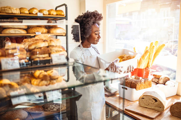 hermosa joven panadero sosteniendo una bandeja de pan en la panadería. - food industry manufacturing human hand fotografías e imágenes de stock