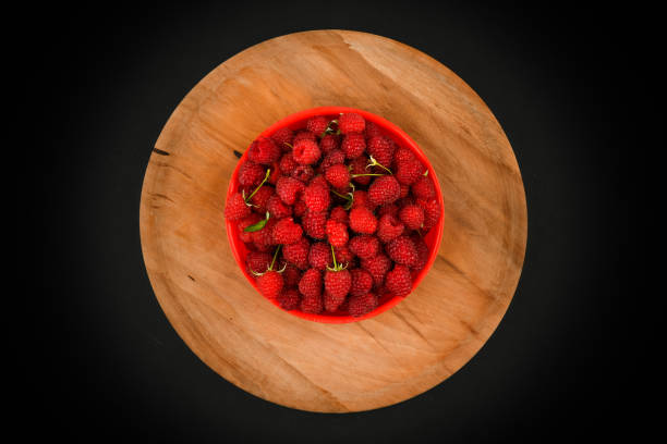 Raspberries on a wooden plate. On a black background close-up. wooden tray. view from above. place for writing. Fresh raspberries on a dark stone background. Close Selective Focus