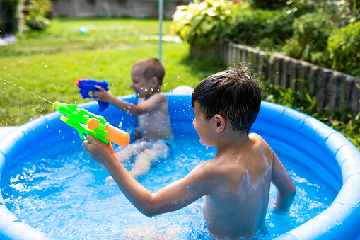 Two cute boys are playing in a paddling pool with water guns