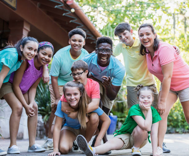 Summer camp including two down syndrome children A happy, multi-ethnic group of children and adults, smiling and looking toward the camera. The girl in the green shirt and boy in the peach-colored shirt wearing eyeglasses both have down syndrome. They are 11 and 12 years old. mixed age range stock pictures, royalty-free photos & images
