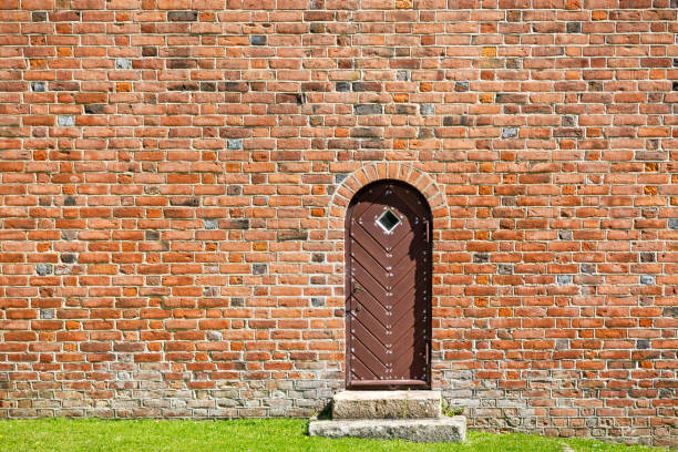 Münster, Nordrhein-Westfalen-Germany - 01-04-2021: Semicircular gate in an old building made of red masonry with a modern bell and a lamp on the facade. The gate is brown and made of boards.