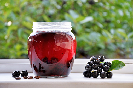 Jar of BlackBerry jam with Ripe blackberries, aronia and coffee beans on window of country house