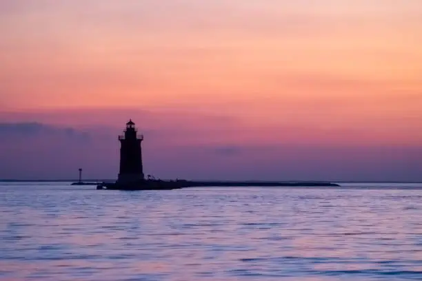 View of a soft sunset reflecting on bay water with lighthouse in background