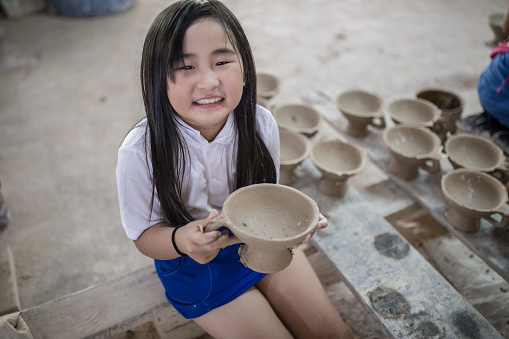 Chinese children is showing finish product of bowl face to camera with smiling face.