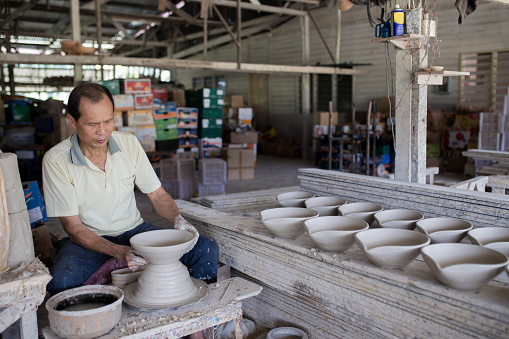 Chinese senior man potter working on pottery wheel while sitting in his workshop