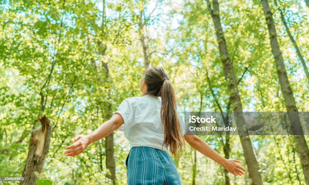 Free woman breathing clean air in nature forest. Happy girl from the back with open arms in happiness. Fresh outdoor woods, wellness healthy lifestyle concept. Nature Stock Photo