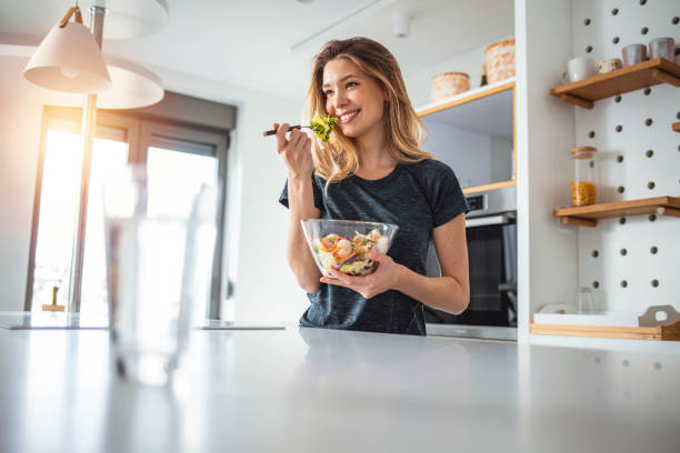 What I eat is who I am Photo of young woman enjoying a delicious salad while standing in her kitchen at home during the day. ladies lunch stock pictures, royalty-free photos & images