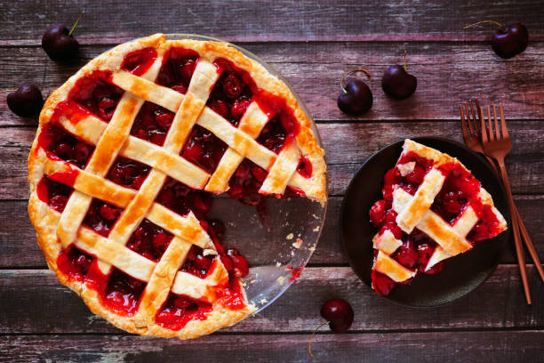 Cherry pie, overhead table scene with cut slice on a wood background
