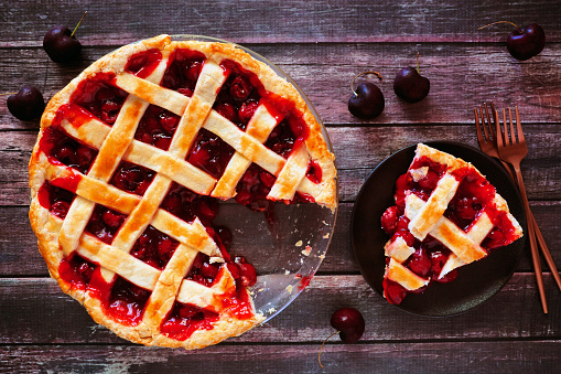 Cherry pie, overhead table scene with cut slice on a rustic wood background. Autumn food concept.