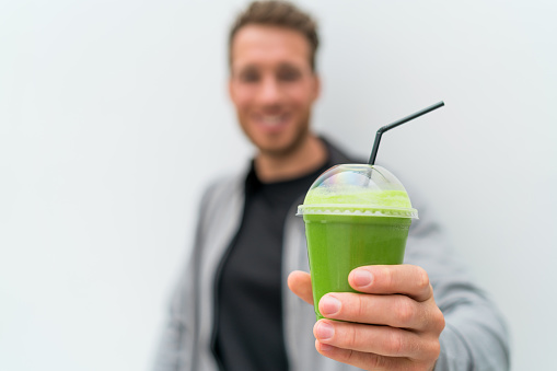 Health man drinking weight loss green smoothie drink. Hand holding plastic cup of vegetable juice, healthy food diet eating lifestyle.