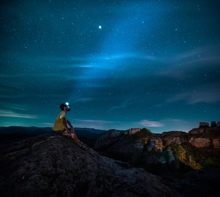 A cheerful solo traveler in the Nature at night contemplating the millions of stars in the dark blue sky. Relaxation Outdoors at the end of the day. Outer space and Astronomy.