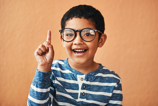 Portrait of an adorable little boy wearing glasses and pointing up with his finger
