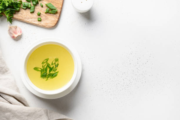 Chicken broth with green onion in white bowl on white table. Copy space. Top view.