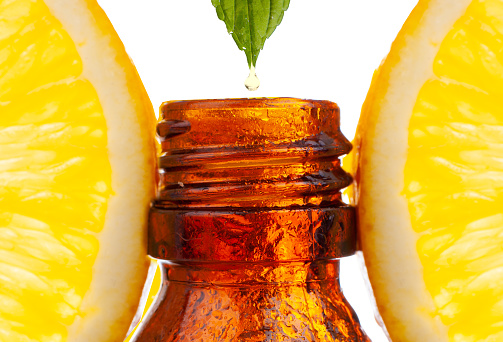 Dripping citrus essential oil into bottle on white background.