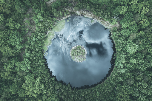 Round lake with island in the middle among forest, aerial view toned colors