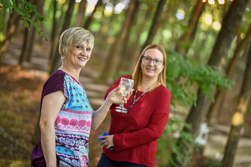 Two woman looking at the camera and toasting in the forest environment.