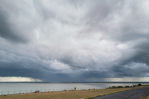 Ramsgate, UK - Aug 28th 2020  Storm clouds over Sandwich bay seen from the west cliff esplanade in Ramsgate. Two people walking on the promenade look tiny against the swell of the cloud.
