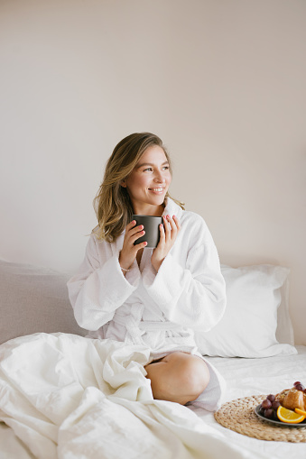 Joven hermosa mujer con bata de baño blanco desayunando en la cama con café y cruasanes y frutas frescas en un dormitorio acogedor. photo