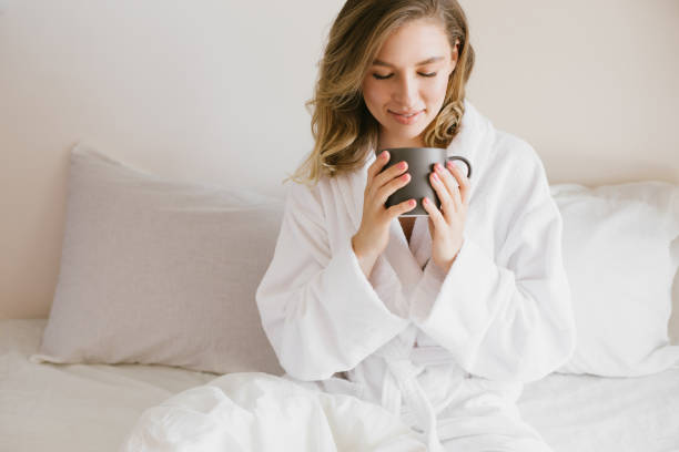 istock Young beautiful woman wearing white bathrobe having breakfast in bed with coffee and croissant and fresh fruits in cozy bedroom. 1269558832