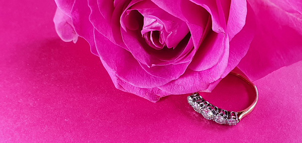 Close up of antique diamond ring with pink rose on pink background