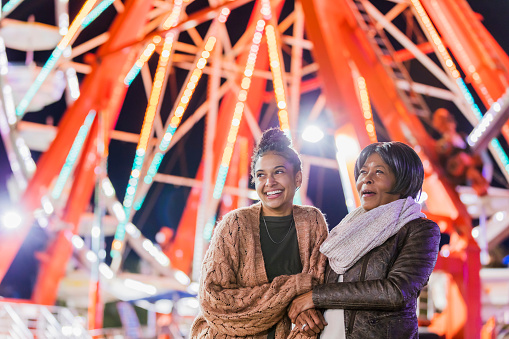 A senior African-American woman in her 60s having fun with her adult granddaughter, a young mixed race African-American and Caucasian woman in her 20s. They are spending the evening at a traveling carnival.