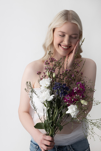 Cheerful pretty lady touching her face and smiling while holding beautiful bouquet