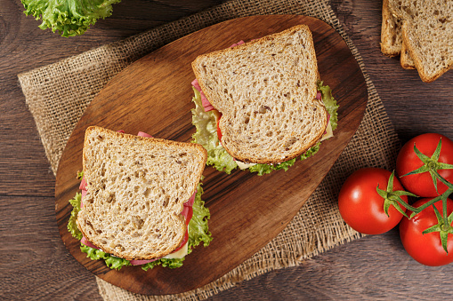 Whole grain bread sandwich with salami, tomato, cheese and fresh lettuce. Top view