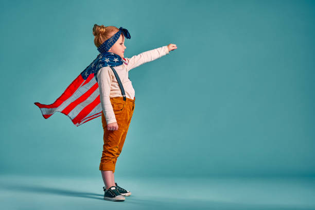 happy independence day. little smiling patriotic girl with an american flag waving in the wind on blue background - child flag fourth of july little girls imagens e fotografias de stock