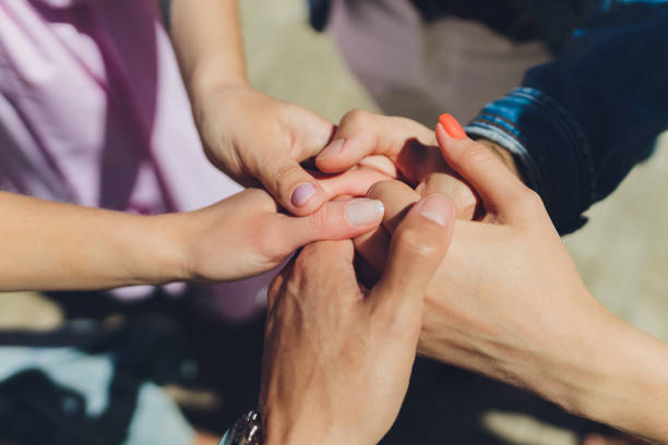 two man and three women holding hands on a table implying a polyamory relationship or love triangle