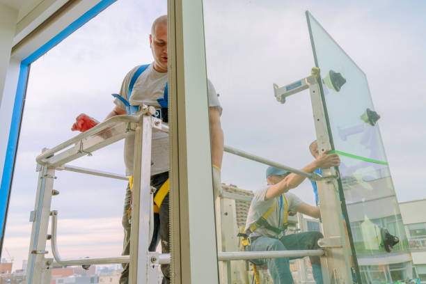 istock Team of blue-collar workers replacing a broken window in the office building - applying a fresh sealant for a new glass installation. High-altitude work on the lifting platform which is placed outside. 1269581619