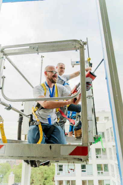 istock Team of blue-collar workers replacing a broken window in the office building - applying a fresh sealant for a new glass installation. High-altitude work on the lifting platform which is placed outside. 1269581621