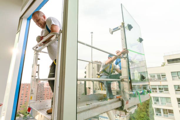 istock Team of blue-collar workers replacing a broken window in the office building - applying a fresh sealant for a new glass installation. High-altitude work on the lifting platform which is placed outside. 1269581622