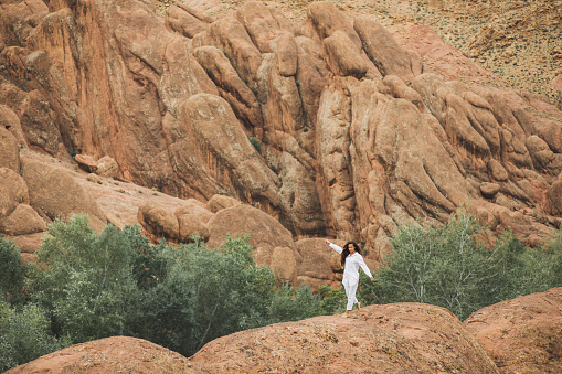 White woman walking on background of Todra gorge canyon landscape in Morocco. Red color mountains formed by weathering.  Travel in Africa. Harmony with nature.