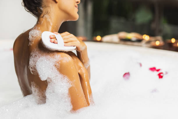woman taking a bath and washing with natural jute sponge. tub with foam bubbles. view from behind.. spa treatment, body care. leisure time. - soap body imagens e fotografias de stock