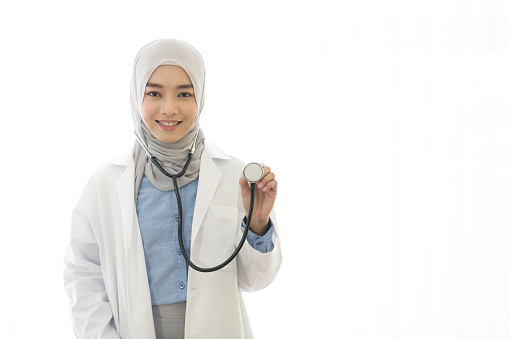 Portrait of Asian muslim female doctor showing stethoscope to camera on white background