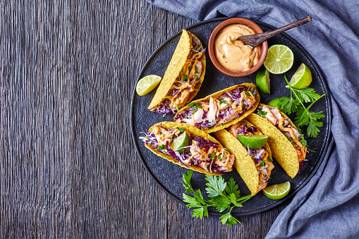 salmon tacos with red cabbage salad with spicy yogurt sauce sprinkled with finely chopped parsley served on a black plate on a dark wooden table, horizontal view from above, flat lay, free space