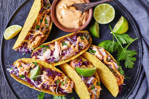 salmon tacos with red cabbage salad with spicy yogurt sauce sprinkled with finely chopped parsley salmon tacos with red cabbage salad with spicy yogurt sauce sprinkled with finely chopped parsley served on a black plate on a dark wooden table, horizontal view from above, flat lay, close-up crunchy photos stock pictures, royalty-free photos & images