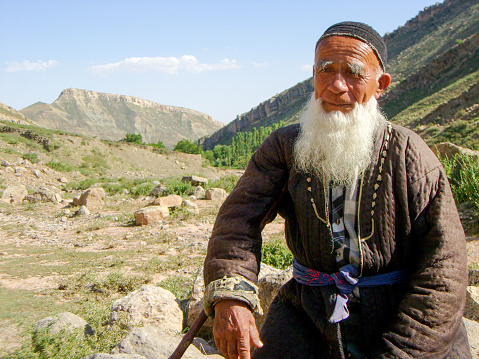 Boysun, Uzbekistan - Jun 8, 2007: The elderly man in traditional Uzbek clothes sitting on a rock in the Boysuntau Mountains.