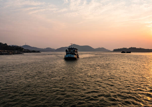 ship heading towards river island at dusk image is taken at peacock island guwahati assam india. it is showing the serene beauty of nature at dusk.