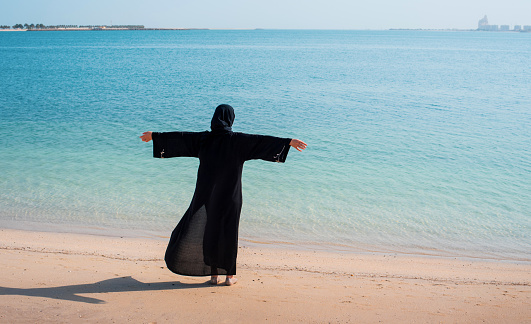 Muslim woman wearing hijab abaya black dress cover on the beach on a sunny day