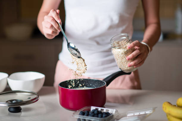 frau macht morgens frühstück haferflocken müsli und zutaten zu hause hinzufügen - oatmeal stock-fotos und bilder