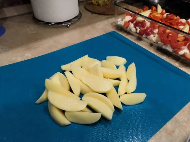 country-style sliced potatoes for baking in the oven, step-by-step process of cooking a vegetable dish on a blue background