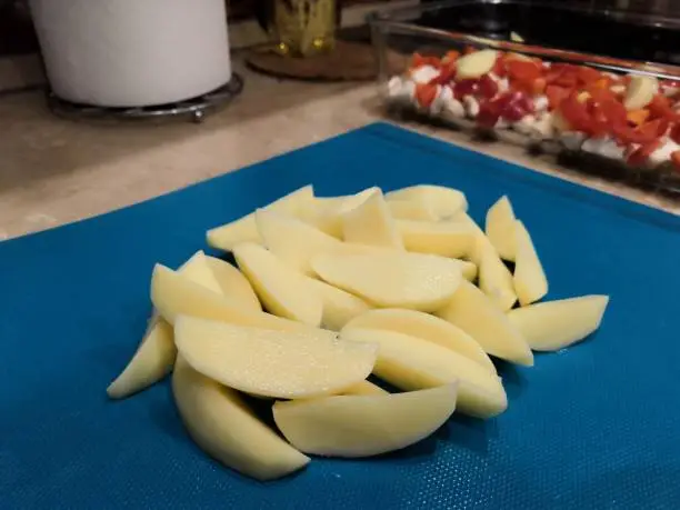 country-style sliced potatoes for baking in the oven, step-by-step process of cooking a vegetable dish on a blue background