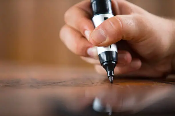 Close-up of a Man Writing or Drawing on Wooden Table With Permanent Marker.
