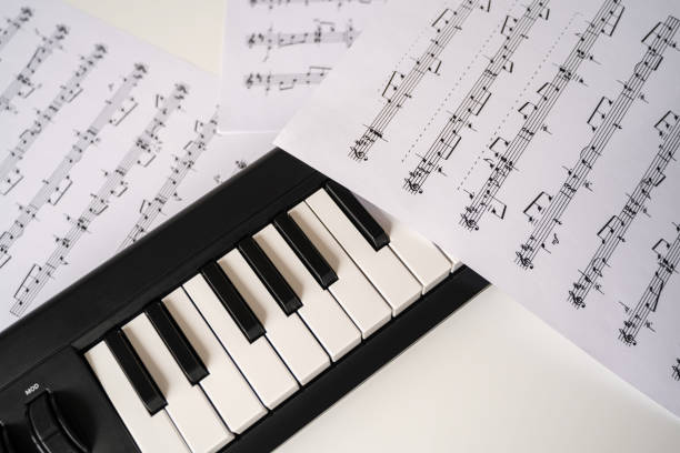 istock Selective focus of home synthesizer with sheet music (musical) notes on a white table. Piano keyboard. 1269656206
