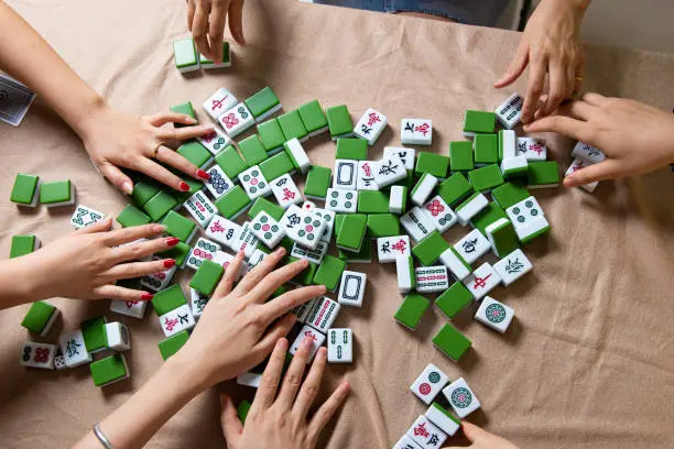 Women mixing tiles while playing Chinese board game Mahjong at home. Fun and leisure with friends, domestic life in Asia