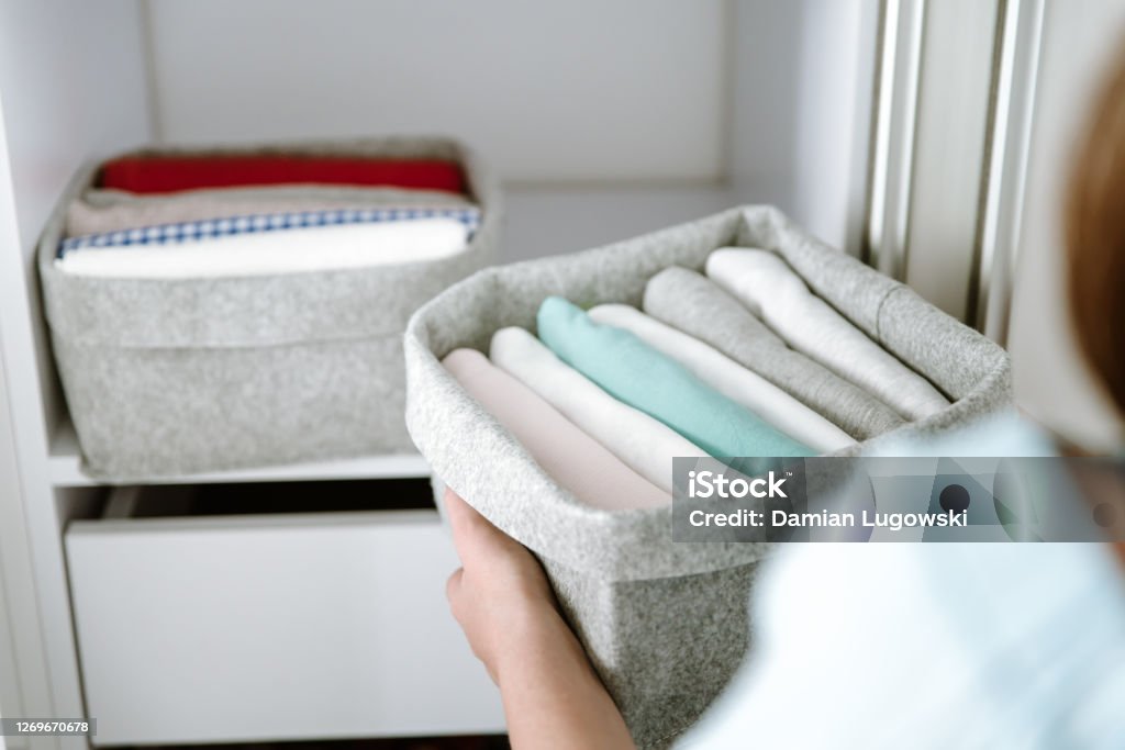 Woman organizing clothes in wardrobe, putting shirts in boxes, baskets into shelves. Clothes neatly folded after laundry. Concept of minimalist lifestyle Woman organizing clothes in wardrobe, putting shirts in boxes. Concept of order, minimalist closet, japanese t-shirt folding system and clothes storage Closet Stock Photo