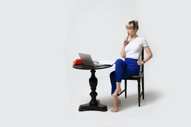 Focused young woman sitting at desk working or studying remotely writing notes while looking on the notebook laptop screen. Distant learning or remote work concept. Isolated on white background. estudiante joven reflexiva sentada en el escritorio trabajando o estudiando remotamente en línea mirando en la pantalla del ordenador portátil con el interés de morder la pluma y el pensamiento. aprendizaje a distancia o trabajo remoto desde casa.