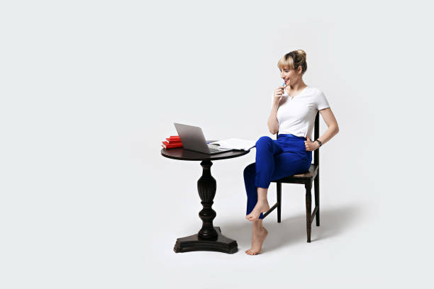 istock Happy smiling young female student sitting at desk working or studying remotely online looking on laptop screen with interest biting pen and thinking. Distant learning or remote work from home. 1269677016