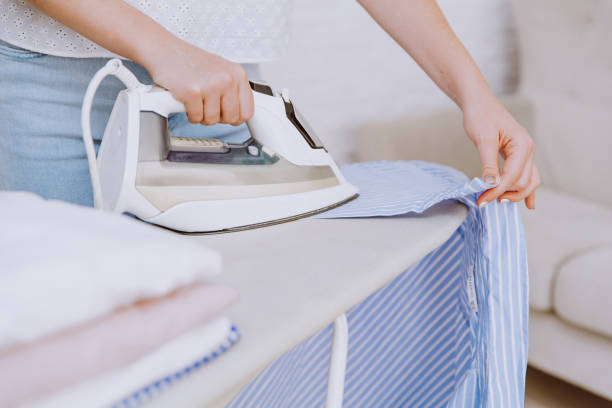 istock Woman ironing blue shirt with steam iron next to stack of folded clothes. 1269677688